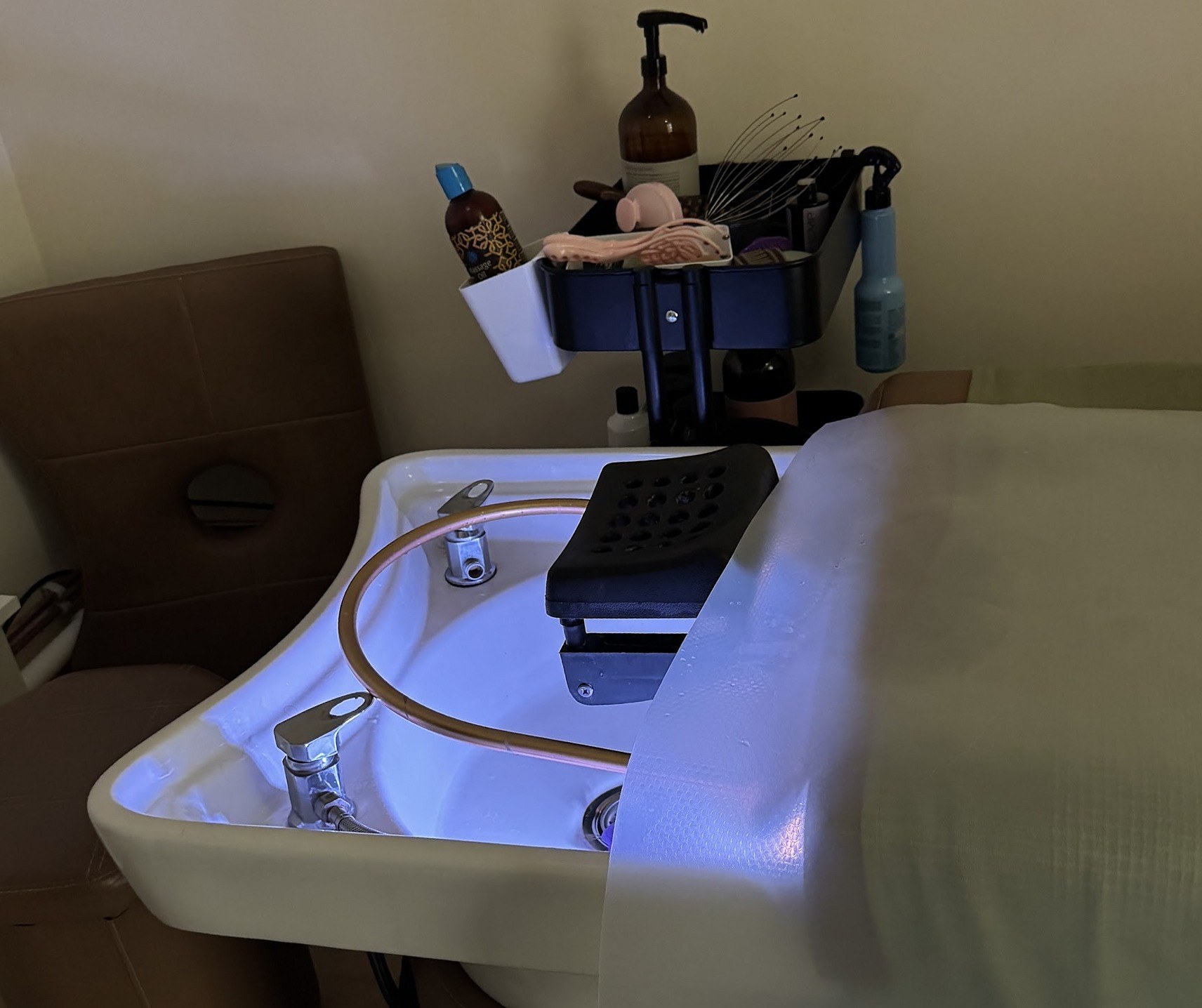 Head spa wasbak met blauw licht, hoofdsteun en een trolley met oliën en massagetools